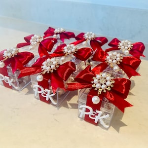May include: Multiple small clear boxes with red bows and pearl embellishments. Each box is decorated with a white label that says "P&K".