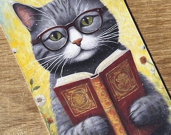 May include: A gray cat wearing glasses sits in a field of flowers and reads a red book with gold accents.
