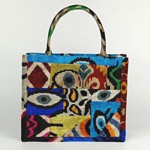 Puede incluir: Una bolsa de mano de patchwork colorida con un patr&oacute;n azul, verde, rojo, amarillo y negro. La bolsa tiene un asa superior y est&aacute; hecha de una tela suave y texturizada.