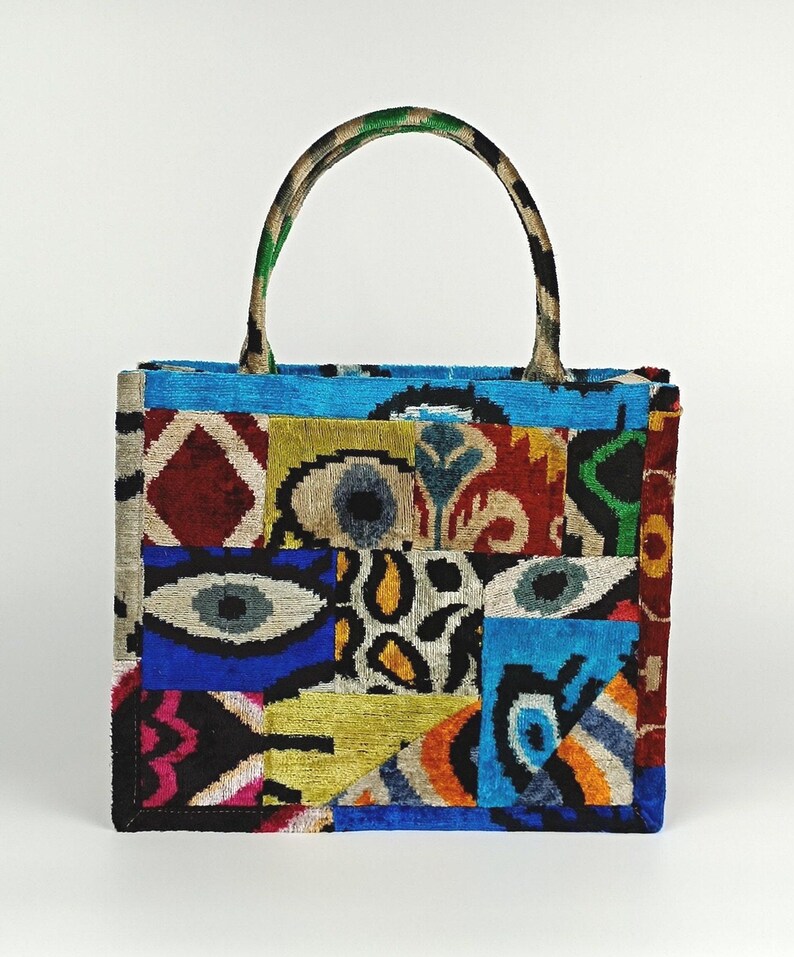 Puede incluir: Una bolsa de mano de patchwork colorida con un patr&oacute;n azul, verde, rojo, amarillo y negro. La bolsa tiene un asa superior y est&aacute; hecha de una tela suave y texturizada.