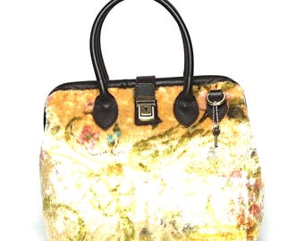 May include: A handbag featuring a plush, textured surface with a cream, yellow, and floral pattern. It includes dark brown leather handles, a matching brown leather trim, and a central metal clasp closure. A small metal key hangs from a side ring.