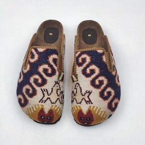 Könnte beinhalten: Paar gemusterte Clogs mit Korkfußbett. Die Clogs haben ein marineblaues und cremefarbenes Design mit roten und orangen Akzenten. Die Größe ist mit 43 angegeben.