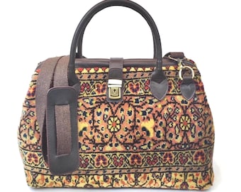 May include: A structured handbag featuring a woven tapestry fabric with a detailed floral and geometric pattern in shades of orange, yellow, and black. The bag includes dark brown leather handles, a matching shoulder strap, and a central metal lock.