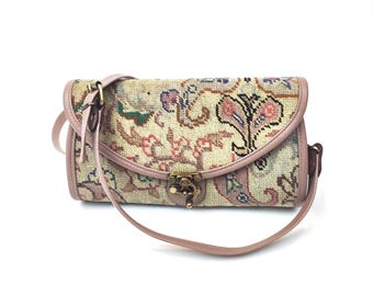 May include: A rectangular shoulder bag featuring a woven tapestry fabric with a multi-colored floral and paisley pattern in shades of pink, green, and blue. The bag has light pink leather trim, a thin shoulder strap, and a brass metal clasp.