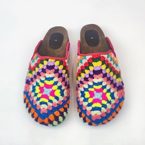 May include: A pair of colorful crochet clogs. The clogs feature a vibrant patchwork design in shades of blue, orange, yellow, pink, purple, and green. The interior is brown with a red trim. The clogs are size 41.