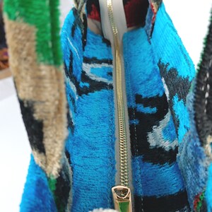 Puede incluir: Primer plano del interior de una bolsa de mano de color azul y negro con una cremallera dorada. La cremallera est&aacute; abierta y el forro es blanco.