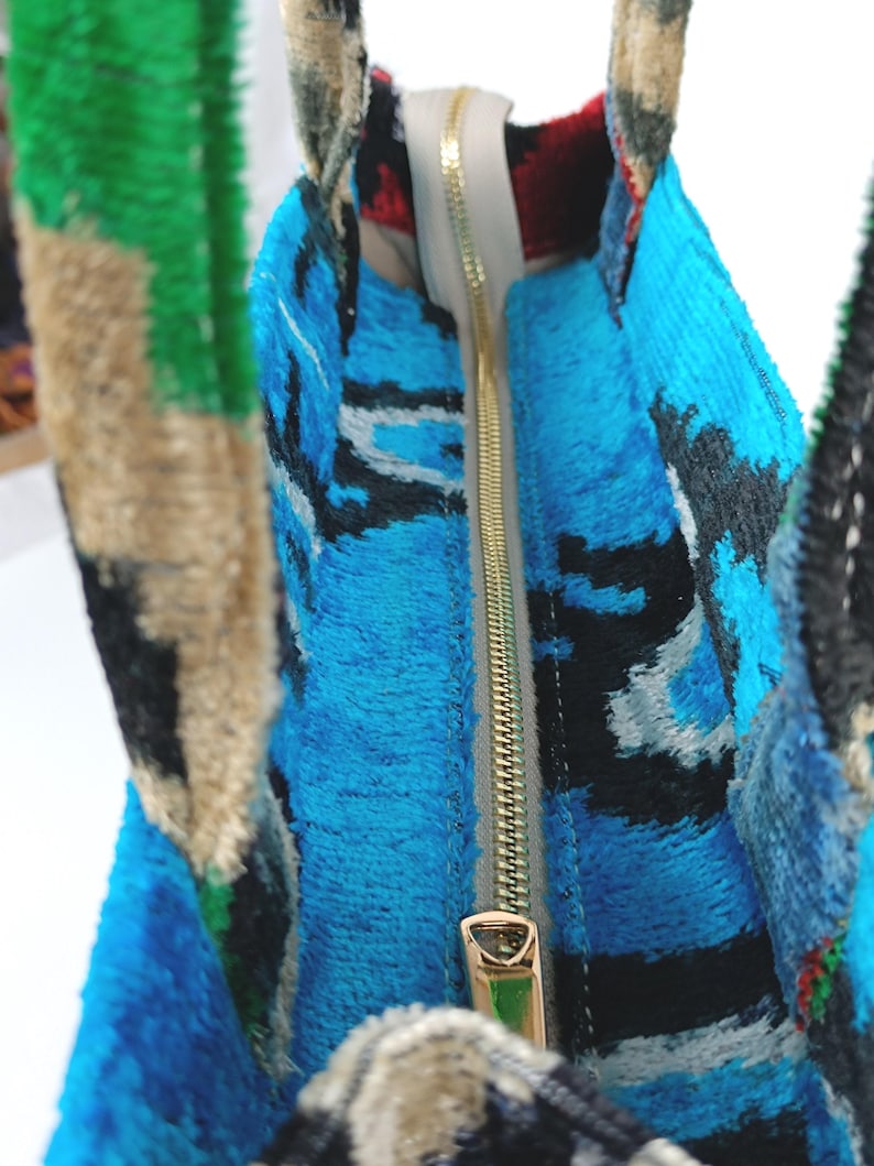 Puede incluir: Primer plano del interior de una bolsa de mano de color azul y negro con una cremallera dorada. La cremallera est&aacute; abierta y el forro es blanco.
