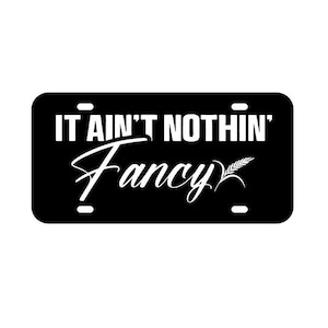 May include: Black and white license plate with the text "It ain't nothin' Fancy" and a small wheat stalk graphic.