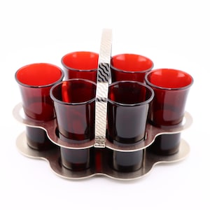 May include: A silver shot glass holder with a handle, holding six red glass shot glasses.