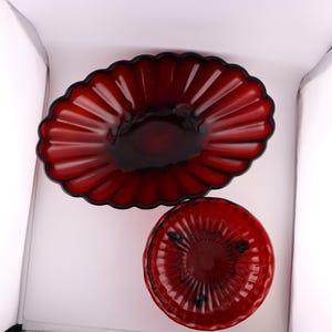 May include: Two red glass bowls, one oval and one round, with a fluted design. The bowls are made of ruby red glass and have a shiny finish.