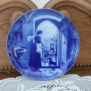May include: Blue and white porcelain plate with a scene of a woman and two children standing in a doorway. The plate has the text "Mother's Day 1992" on the bottom.