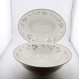May include: Two white ceramic bowls with a floral design. The bowls have a gold rim and a delicate floral pattern in shades of green, brown, and blue.