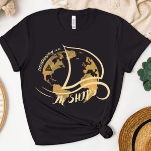 May include: Black t-shirt with a gold graphic of a globe with the text "Decononomy is in ships" on it.