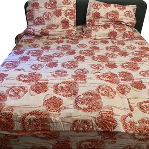 Op de afbeelding: Een wit bed met een rood, bloemig patroon duvet cover en bijpassende kussenslopen. Het bed heeft een donkergrijze hoofdeinde.