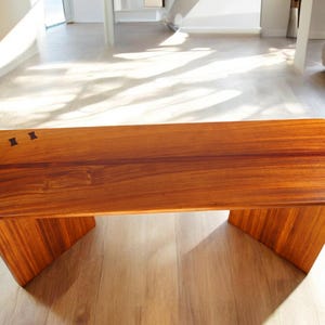Può includere: Un tavolino da caffè in legno con finitura in legno naturale. Il tavolo ha un piano rettangolare e un design semplice e moderno. Il tavolo è realizzato in legno massello e ha una superficie liscia e lucida.