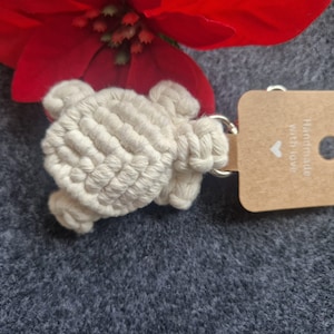 Könnte beinhalten: Ein weißer gehäkelter Schildkröten-Schlüsselanhänger mit einem braunen Etikett, auf dem "Handmade with love" und ein kleines Herz steht.