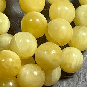 Peut inclure: Gros plan sur une collection de perles rondes jaunes. Les perles ont une surface lisse et polie et varient légèrement en teinte, du pâle au jaune plus foncé. Les perles sont dispersées, créant un motif texturé et organique.