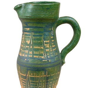 Peut inclure: Pichet en céramique verte avec bec et anse. Le pichet présente un motif décoratif bleu et beige, avec une base large et un col plus étroit. La anse est incurvée et le pichet a un aspect rustique et fait à la main.