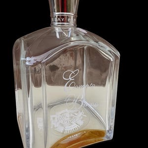 Peut inclure: Flacon de parfum en verre transparent avec un bouchon argenté. Le flacon a une forme géométrique et contient un liquide de couleur claire. Le flacon porte les mots "Compto Bromo" gravés sur le devant.