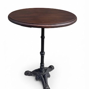 May include: A round table with a dark brown wooden top and a black metal pedestal base. The base features a central column with decorative detailing and three ornate, curved legs that extend outwards to provide stability for the tabletop.