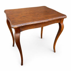 Peut inclure: Petite table d'appoint en bois antique, avec un plateau carré et des pieds courbés. La table est en bois aux tons chauds, probablement du chêne, et présente un bord légèrement festonné. Les pieds sont gracieusement courbés, ajoutant au charme vintage.