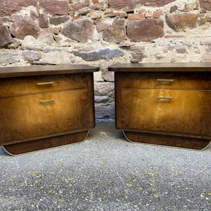 Puede incluir: Dos mesitas de noche de madera con dos cajones cada una. Las mesitas de noche tienen un acabado marrón oscuro y una base curva. Los cajones tienen tiradores de latón.