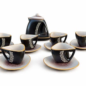 Könnte beinhalten: Schwarzes und weißes Keramik-Teeservice mit Teekanne und sechs Tassen und Untertassen. Die Tassen und die Teekanne haben ein geometrisches weißes Design. Die Untertassen haben einen hellbraunen und goldenen Rand.
