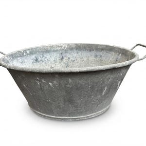 May include: A round, galvanised metal basin with a weathered, mottled grey finish. The basin features a wide, open top, a tapered body, and two rectangular metal handles attached to opposite sides of the rim for lifting and carrying purposes.