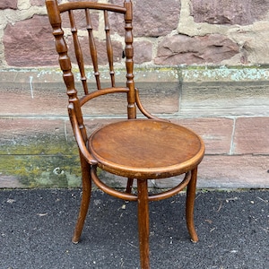 Può includere: Una sedia in legno con un sedile rotondo e uno schienale alto a doghe. La sedia è realizzata in legno marrone chiaro e ha un design semplice e classico.