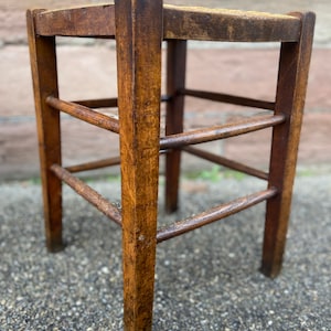 Puede incluir: Un taburete de madera con tres estantes. El taburete es de madera marrón oscuro y tiene una parte superior cuadrada.