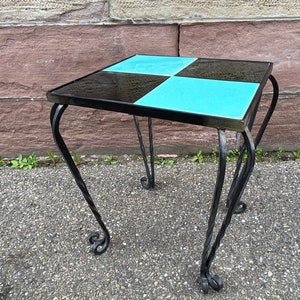 Peut inclure: Une petite table d'appoint carrée avec un plateau en carreaux noirs et turquoise et des pieds en fer forgé noir.