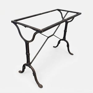 May include: A rectangular table base constructed from dark brown metal. The frame features a flat top perimeter supported by two vertical legs that branch into curved feet at the bottom, connected by a central cross-brace structure for stability.