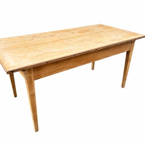 Puede incluir: Una mesa rectangular de madera con un acabado en tono bronceado claro y veta de madera visible. La mesa presenta una superficie superior plana, un faldón recto a lo largo de los lados y cuatro patas cónicas que se extienden hacia abajo.