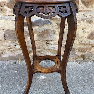 Peut inclure: Un support de plante en bois antique brun foncé avec un dessus rond et des motifs floraux sculptés. Le support a quatre pieds incurvés et une étagère inférieure décorative. Le support mesure environ 61 cm de haut.
