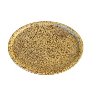 以下が含まれることがあります： 黄色と茶色の色合いの、丸い斑点模様のトレイ。トレイにはわずかに盛り上がった縁とテクスチャ加工された表面があります。 全体的なデザインはシンプルで素朴で、サービングやディスプレイに適しており、直径は約30cmです。