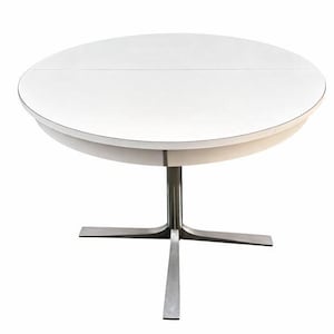Könnte beinhalten: Ein weißer, runder Esstisch mit einem Sockel aus Edelstahl. Die Tischplatte scheint aus einem glatten, festen Material zu bestehen. Der Tisch hat einen Durchmesser von ca. 122 cm.