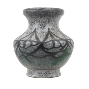 May include: A ceramic vase with a speckled gray and green finish. The vase features a black, stylized floral design around the middle and the text "Saint Clement" at the base. The vase has a rounded body and a flared rim.