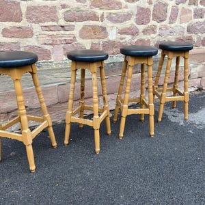 Könnte beinhalten: Vier Holz-Barhocker mit schwarzen gepolsterten Sitzen. Die Hocker haben ein schlichtes Design mit vier Beinen und einer quadratischen Sitzfläche.