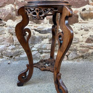 Könnte beinhalten: Ein dunkelbrauner Holz-Beistelltisch mit aufwendigen Schnitzereien und einer runden Tischplatte. Der Tisch hat drei Beine mit einem geschwungenen Design.