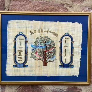 May include: A framed piece of papyrus art depicting a tree of life with colorful birds and hieroglyphics. The text on the papyrus reads "2000".