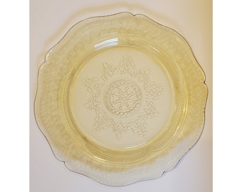 May include: A yellow glass plate with a raised, intricate design. The plate has a scalloped edge and a central design with a starburst pattern.