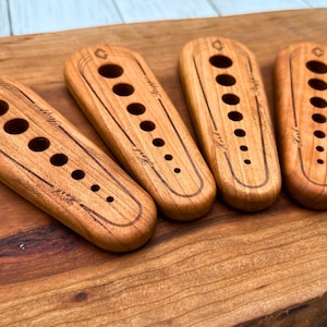 May include: Four wooden tools with different sized holes, each with the word "Knit" engraved on them. The tools are arranged in a row on a wooden surface.