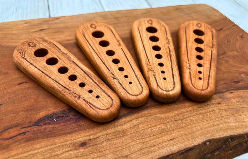 May include: Four wooden tools with different sized holes, each with the word "Knit" engraved on them. The tools are arranged in a row on a wooden surface.