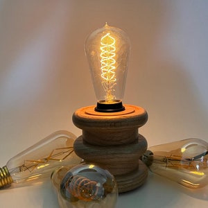 May include: A wooden lamp base with a warm, glowing Edison bulb. The base has a stacked design with three rings. There are three additional Edison bulbs on the table.