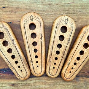 May include: Four wooden tools with holes and the text "First" and "Stripper" engraved on them. The tools are arranged in a semi-circle on a wooden surface.