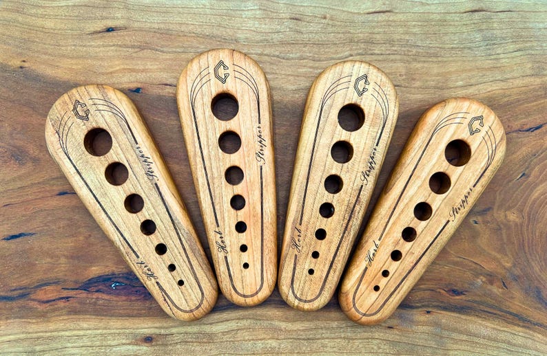 May include: Four wooden tools with holes and the text "First" and "Stripper" engraved on them. The tools are arranged in a semi-circle on a wooden surface.