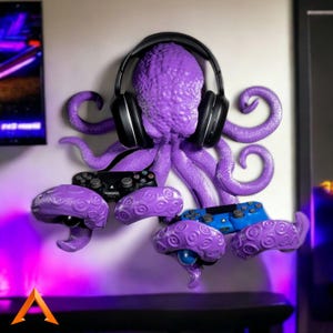May include: A purple octopus-shaped wall mount for gaming accessories. The octopus holds a black headset and has multiple tentacles designed to hold game controllers. The wall mount is a vibrant purple color.