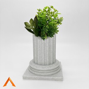 May include: A white ceramic planter shaped like a column with a base and a top rim. The planter is filled with green leafy plants.
