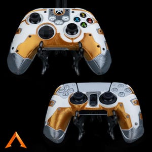 Könnte beinhalten: Zwei individuell gestaltete Videospiel-Controller, einer weiß und gold mit Xbox-Tasten, und einer weiß und gold mit PlayStation-Tasten.
