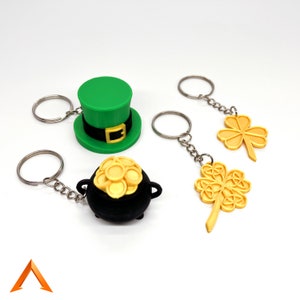Puede incluir: Cuatro llaveros con un sombrero de duende verde, una olla de oro llena de monedas y dos diseños de trébol de cuatro hojas dorados. Los llaveros están todos unidos a llaveros de plata.